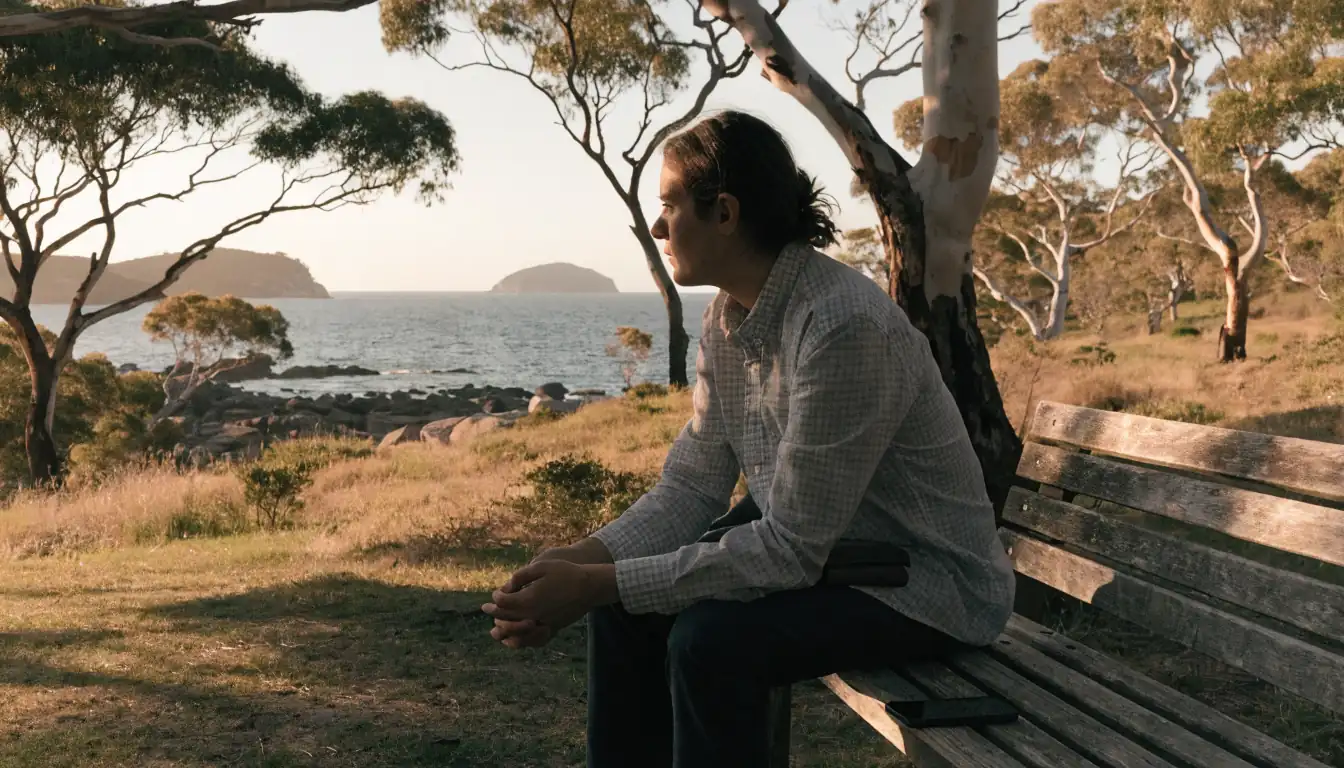 A thoughtful person sits on a coastal park bench in Australia with phone face-down, reflecting on gambling habits at sunset.
